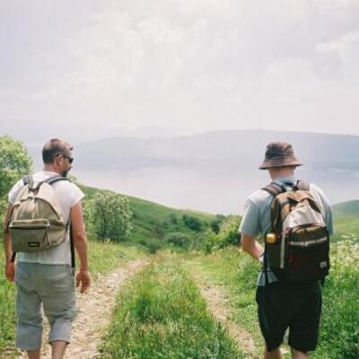 Deux hommes avec des sacs à dos marchent sur un chemin bordé de verdure, illustrant les activités en plein air organisées par l'association des étudiants en ostéopathie