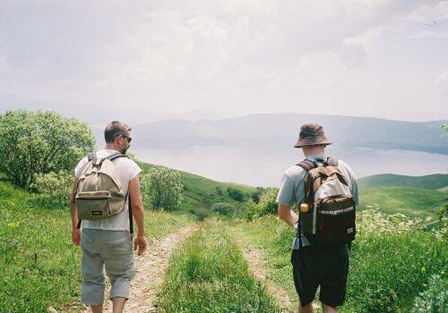 Deux hommes avec des sacs à dos marchent sur un chemin bordé de verdure, illustrant les activités en plein air organisées par l'association des étudiants en ostéopathie