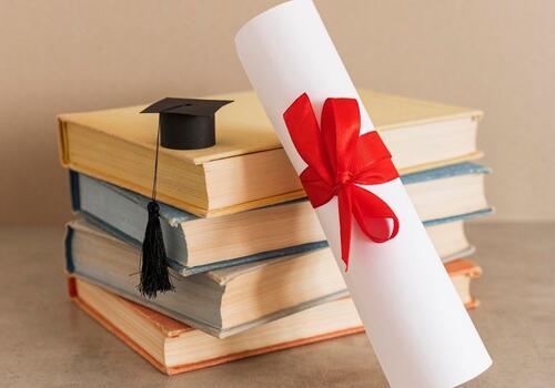 Un chapeau et un diplôme de fin d'études reposant sur une pile de livres, symbolisant la réussite scolaire et le succès.
